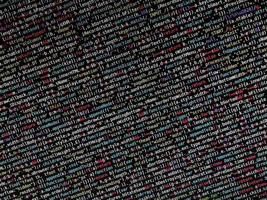 Close-up photograph of a computer screen displaying lines of computer code in various colors, including red, green, yellow, blue, and white, on a black background. The code consists of syntax highligh